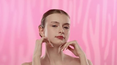 Açık tenli genç bir kadın nazikçe yüzüne dokunuyor, cilt teması ve gençlik ışıltısı öneriyor..