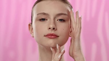 Açık tenli genç bir kadın nazikçe yüzüne dokunuyor, cilt teması ve gençlik ışıltısı öneriyor..