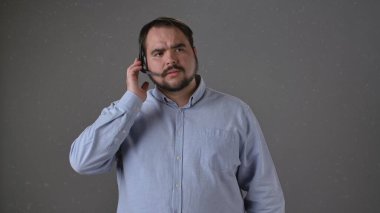 Açık mavi gömlekli bir adam gri arka planda kulaklıkla konuşuyor, odaklandığını ve olaya dahil olduğunu ifade ediyor. Çağrı Merkezi Kavramı.