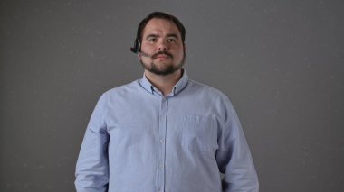 Açık mavi gömlekli kendine güvenen bir adam profesyonel bir kulaklık takar, sade bir arka fonda durur..