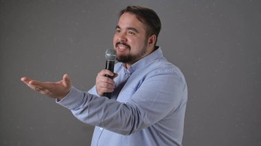 Kendine güvenen bir konuşmacı bir mikrofon tutuyor, seyirciye tutkulu bir şekilde işaret ediyor..