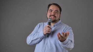 Kendine güvenen bir konuşmacı bir mikrofon tutuyor, seyirciye tutkulu bir şekilde işaret ediyor..