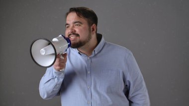 Mavi gömlekli bir adam megafonla konuşuyor, sesli iletişim ve duyuruları vurguluyor..