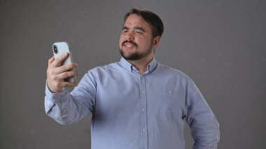 Mavi tişörtlü bir adam gülümseyip el sallarken akıllı telefonuyla videoyu arıyor..