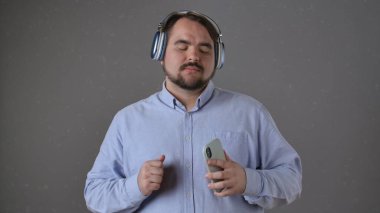 Açık mavi gömlekli bir adam kulaklıkla müzik dinler, akıllı telefon tutar, gözleri kapalı, rahatlamış hisseder..