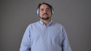 Açık mavi bir gömlek ve kulaklık takan bir adam tarafsız bir arkaplanda duruyor..