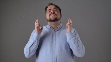 Açık mavi gömlekli bir adam gözleri kapalı, parmakları çapraz durarak, umut dile ya da şans dile..