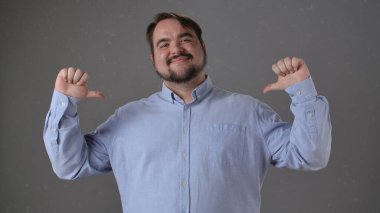 Mavi gömlekli, kendine güvenen, gülümseyen ve kendini gösteren, gururunu ya da başarısını ifade eden bir adam..