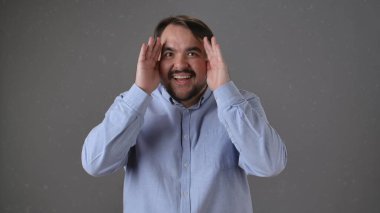 Mavi gömlekli neşeli bir adam ellerini göz teması kurmak için kullanır. Heyecan ve neşe ifade eder..
