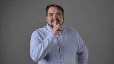 Açık mavi gömlekli bir adam, dudaklarına bir parmak bastırarak sessizlik talep ediyor..