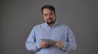 Mavi tişörtlü bir adam arka planda odaklanmış bir ifadeyle parayı tutuyor ve sayıyor..