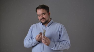 Mavi tişörtlü bir adam arka planda odaklanmış bir ifadeyle parayı tutuyor ve sayıyor..