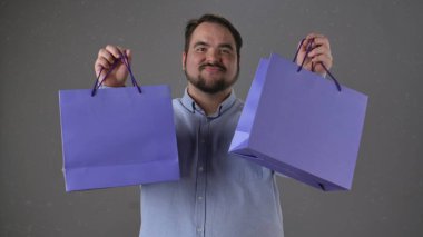 Gülümseyen bir adam renkli alışveriş torbalarını dostça sunar. Görüntü neşe ve memnuniyet verir..