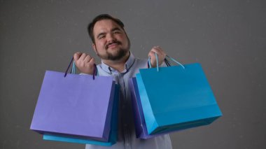 Gülümseyen bir adam renkli alışveriş torbalarını dostça sunar. Görüntü neşe ve memnuniyet verir..