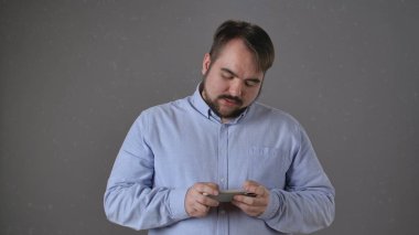 Mavi gömlek giyen bir kişi dikkatle taşınabilir bir cihaza odaklanır, konsantrasyon duygusunu iletir..