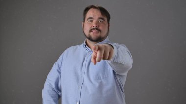 Açık mavi gömlekli bir adam parmağını doğrudan kameraya doğrultarak işaret eder ve vurgu yapar..