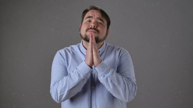 Açık mavi gömlekli bir adam umut dolu ve yalvaran bir yüz ifadesi sergiliyor..