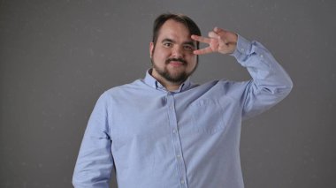 Açık mavi gömlekli bir adam tarafsız bir arkaplanda barış işareti gösteriyor, pozitiflik taşıyor..
