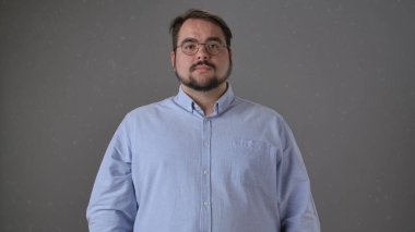 Açık mavi gömlekli, arka planda gözlük takan bir adamın portresi. Görüntü sakin bir ifadeyi yakalar.