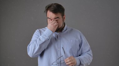 Mavi gömlekli sakallı bir adam. Hüsran içinde gözlerini ovalıyor. Yorgunluk ve stresi simgeliyor..