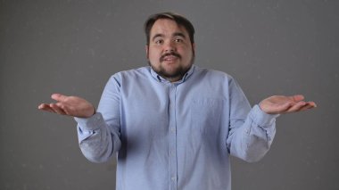 Açık mavi gömlekli bir adam iki eli havada, omuz silkiyor. Kararsız ya da kafası karışık görünüyor..