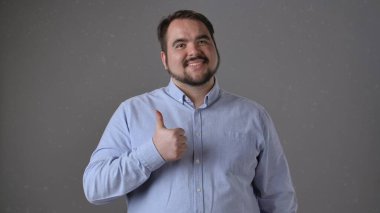 Mavi gömlekli neşeli bir adam başparmağıyla işaret verirken gülümsüyor, pozitifliğini iletiyor..