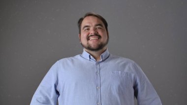 Açık mavi gömlekli bir adam, tarafsız bir arkaplana gülümsüyor, mutluluk ve sıcaklık saçıyor..