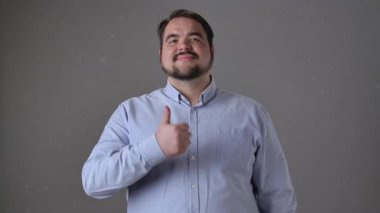 Mavi gömlekli neşeli bir adam başparmağıyla işaret verirken gülümsüyor, pozitifliğini iletiyor. Yavaş çekim