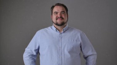 Açık mavi gömlekli bir adam açık ağızla heyecan sergiliyor ve gri bir arkaplana karşı ellerini kaldırıyor. Yavaş çekim