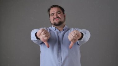 Mavi gömlekli bir adam, tarafsız bir arkaplana karşı baş parmak işareti yaparak onaylamadığını gösterir. Yavaş çekim