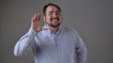 Mavi gömlekli bir adam eli kulağının yanında hareket ediyor, dikkatle dinlediğini gösteriyor. Yavaş çekim