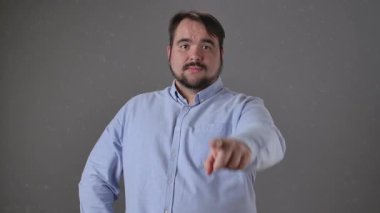 Açık mavi tişört giyen bir adam parmağını doğrudan kameraya doğrultarak işaret eder ve vurgu yapar. Yavaş çekim