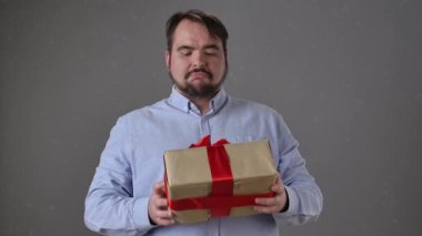 Mavi gömlekli bir adam, parlak kırmızı bir kurdeleyle sarılı bir hediye kutusunu inceliyor ve merak uyandırıyor. Yavaş çekim