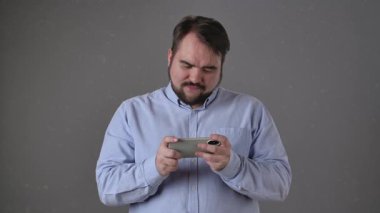 Açık mavi tişörtlü bir adam iki eliyle bir akıllı telefon tutuyor, mobil oyun oynarken hayal kırıklığını gösteriyor. Yavaş çekim