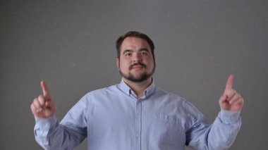 Mavi gömlekli bir adam gülümsüyor ve iki parmakla işaret ediyor, muhtemelen yararlı bir fikir veya öneriyi işaret ediyor..