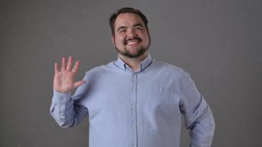 Açık mavi gömlekli bir adam, basit bir gri arka plana gülümsüyor, sıcaklığı ve dostluğu iletiyor..