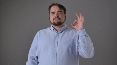 Açık mavi gömlekli bir adam tarafsız bir arkaplana karşı iyi bir hareket gösteriyor. Kendinden emin ve sakin görünüyor..