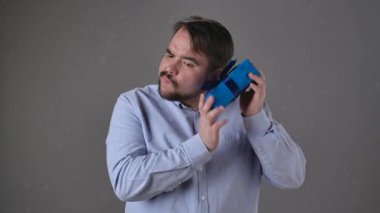 Mavi gömlekli bir adam, parlak mavi bir kurdeleyle sarılı bir hediye kutusunu inceliyor..