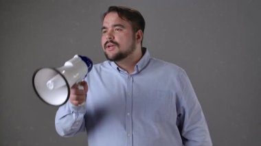 Mavi gömlekli bir adam megafonla konuşuyor, sesli iletişim ve duyuruları vurguluyor..