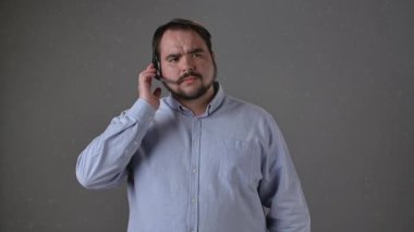 Açık mavi gömlekli bir adam gri arka planda kulaklıkla konuşuyor, odaklandığını ve olaya dahil olduğunu ifade ediyor. Çağrı Merkezi Kavramı.