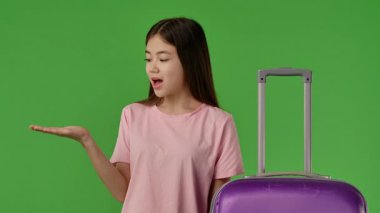 Mor bavulun yanında duran pembe tişörtlü genç kız avucunun içine bakıyor, fotokopi odası. Krom anahtar yeşil ekran yeşil ekran stüdyo arka plan modelinde izole edilmiş. Yavaş çekim