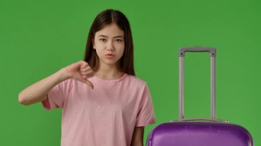Pembe gömlekli genç kız mor bavulun yanında duruyor ve baş parmak işareti yapıyor. Krom anahtar yeşil ekran yeşil ekran stüdyo arka plan modelinde izole edilmiş. Yavaş çekim