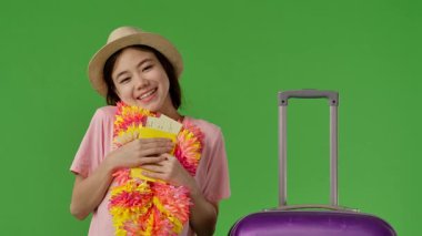 Çiçekli genç kız mor bavulun yanında duruyor ve göğsüne uçak biletleriyle pasaportunu sıkıca tutuyor. Krom anahtar yeşil ekran yeşil ekran stüdyo arka plan modelinde izole edilmiş. Yavaş çekim