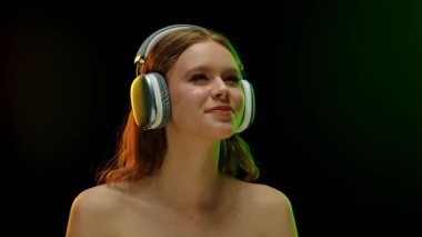 Gözleri kapalı bir kadın, kulaklık takıyor, müziğe dalmış, karanlık bir arka plana karşı..