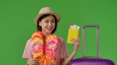 Çiçekli çiçek desenli bavulun yanında elinde biletlerle pasaport tutan ve baş parmak işareti yapan genç bir kız. Krom anahtar yeşil ekran yeşil ekran stüdyo arka plan modelinde izole edilmiş. Yavaş çekim