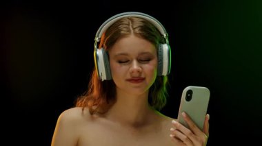 Gözleri kapalı bir kadın, kulaklık takıyor, müziğe dalmış, karanlık bir arka plana karşı..