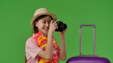 Çiçekli genç kız mor bavulun yanında elinde retro kamerayla duruyor. Krom anahtar yeşil ekran yeşil ekran stüdyo arka plan modelinde izole edilmiş. Yavaş çekim