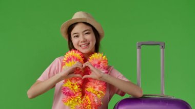 Çiçekli genç kız mor bavulun yanında duruyor ve elleriyle kalp işareti gösteriyor. Krom anahtar yeşil ekran yeşil ekran stüdyo arka plan modelinde izole edilmiş. Yavaş çekim
