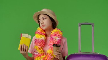 Çiçekli genç kız mor bavulun yanında duruyor, elinde pasaportu ve uçak biletleri var ve kahve içiyor. Krom anahtar yeşil ekran yeşil ekran stüdyo arka plan modelinde izole edilmiş. Yavaş çekim