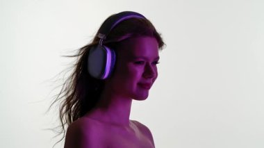 Gözleri kapalı genç bir kadın, duyusal bir deneyime dalmış, büyük kulaklıklarla müzik dinler. Yavaş çekim